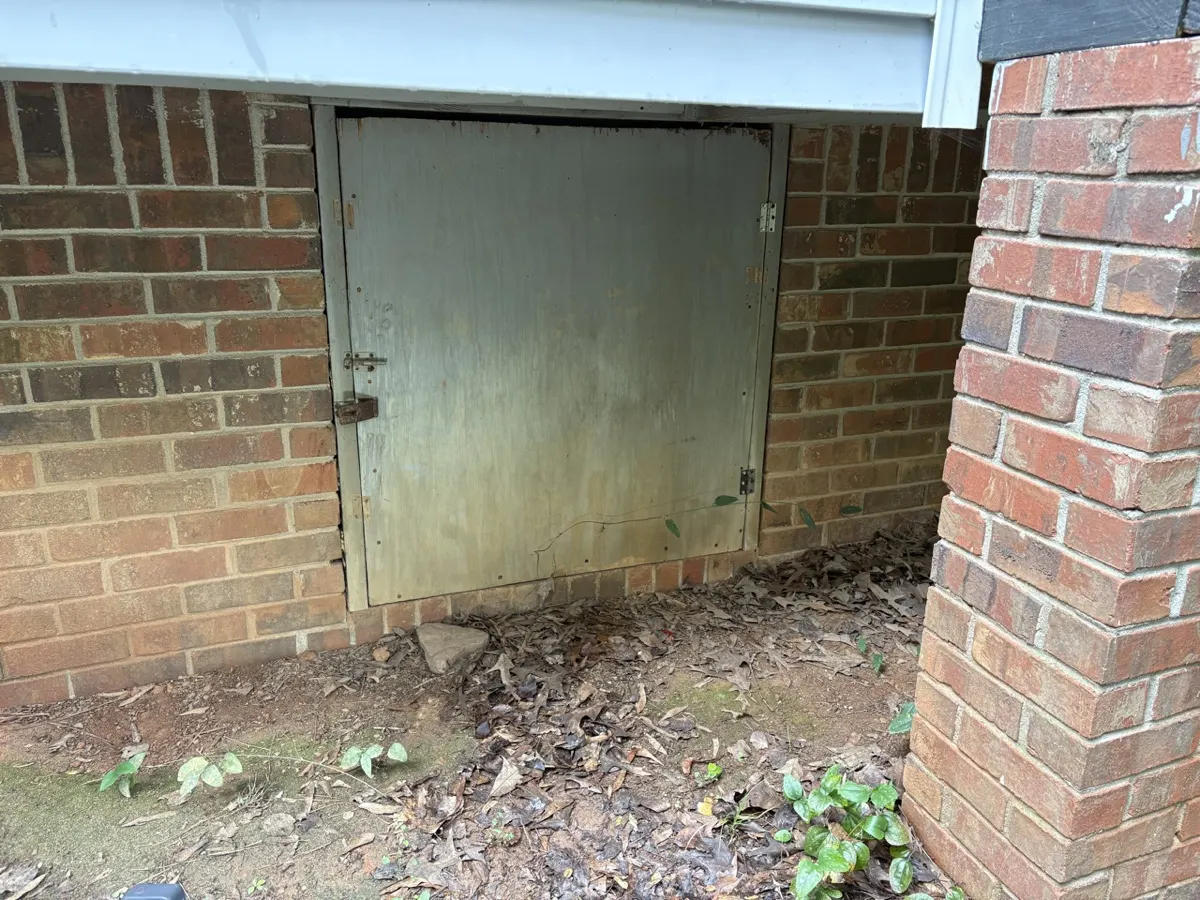 A closed crawlspace access door in a brick home foundation
